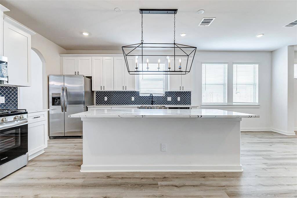 Storage and style come together in this modern kitchen, featuring ample cabinetry, a stainless steel refrigerator, and stunning quartz countertops. The spacious design and large windows ensure this space remains bright and inviting, making meal prep and entertaining a breeze. **This is a picture of a Rylan Floor Plan from another Saratoga Homes.**