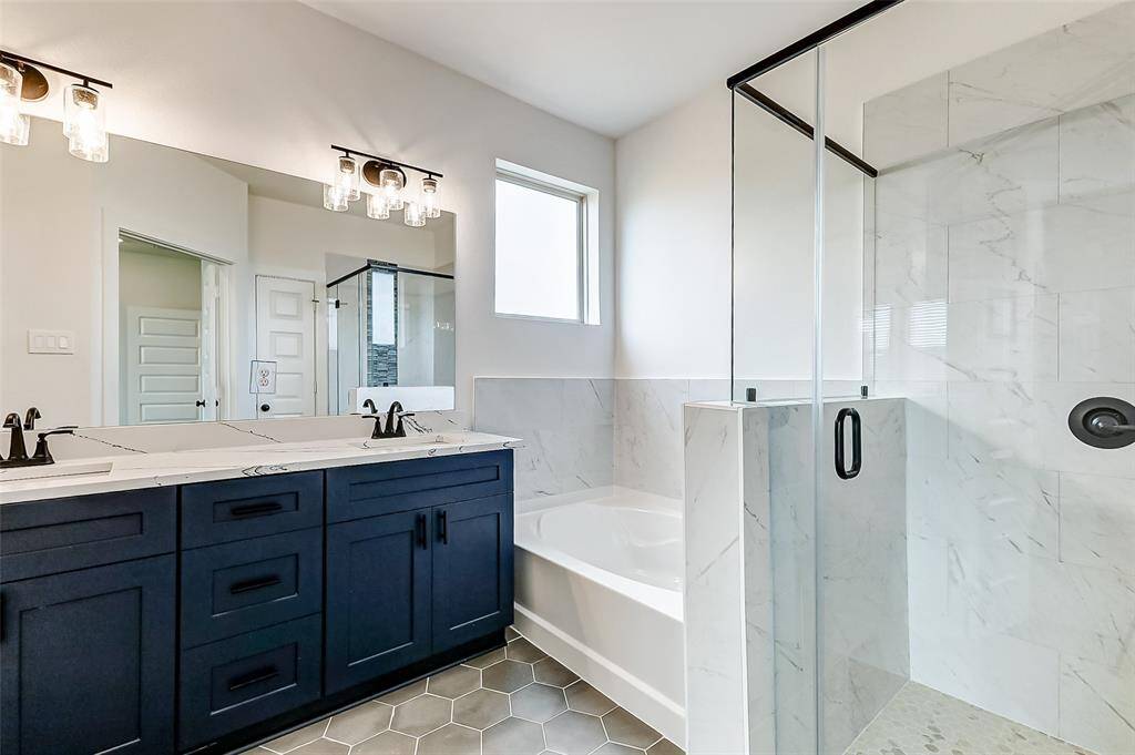 This ensuite features dual vanities, a glass-enclosed shower, a deep soaking tub, and elegant navy cabinetry. A tranquil space to unwind and recharge. This is a picture of a Rylan Floor Plan from another Saratoga Homes.