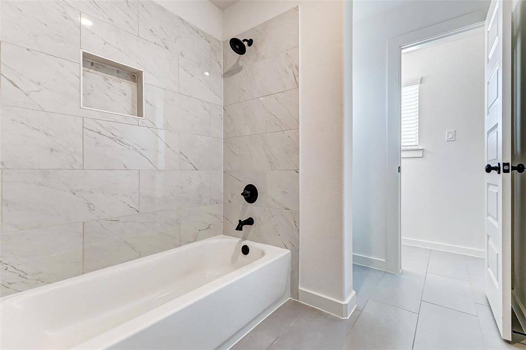 Relax in a beautifully tiled tub and shower combination featuring sleek black fixtures, a built-in niche, and modern finishes. The adjoining bright hallway leads to additional private spaces for your convenience. **This is a picture of a Rylan Floor Plan from another Saratoga Homes.**