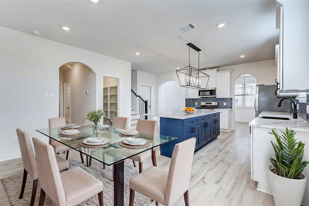 A chef’s dream! This gorgeous kitchen features an oversized quartz island with navy cabinetry, white shaker cabinets, and a stylish backsplash. Stainless steel appliances, a deep farmhouse sink, and modern black hardware add an elegant touch. Open to the living area, this kitchen is designed for hosting and everyday convenience. **This is a picture of a Rylan Floor Plan from another Saratoga Homes.**