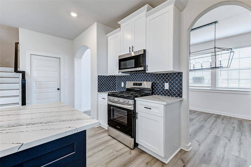 Sleek and modern, this kitchen showcases a stylish blue-tiled backsplash, marble-inspired quartz countertops, and high-end stainless steel appliances. The combination of white and navy cabinetry adds a pop of contrast, while oversized pendant lighting completes the contemporary aesthetic. A perfect blend of beauty and function! **This is a picture of a Rylan Floor Plan from another Saratoga Homes.**