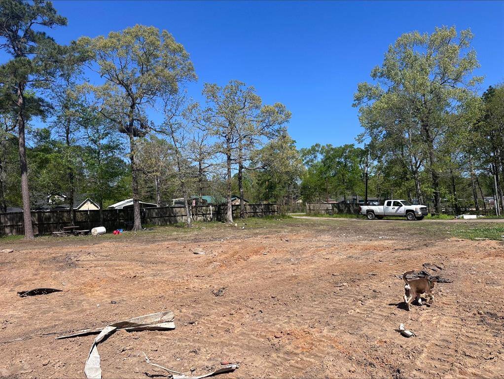 Spacious, cleared lot with mature trees along the perimeter, offering privacy. Includes a fenced boundary and a driveway with a parked truck, suitable for building a new home.
