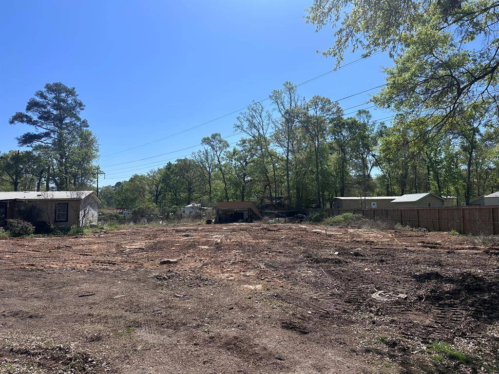 Cleared land ready for development, surrounded by trees and a few neighboring structures. Ideal for building a new home in a serene, natural setting.