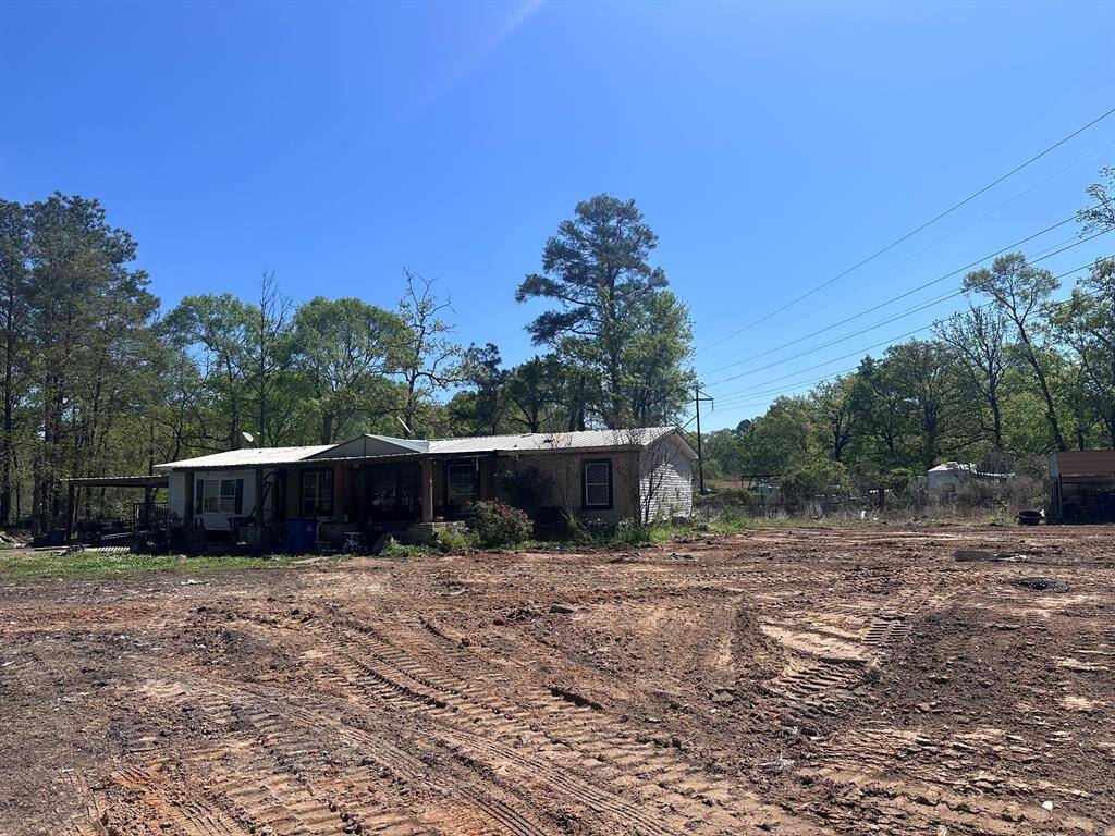 This photo shows a modest single-story home with a metal roof, set on a spacious, cleared lot. The property is surrounded by trees, providing a natural, rural feel. Ideal for buyers seeking a quiet, secluded location.