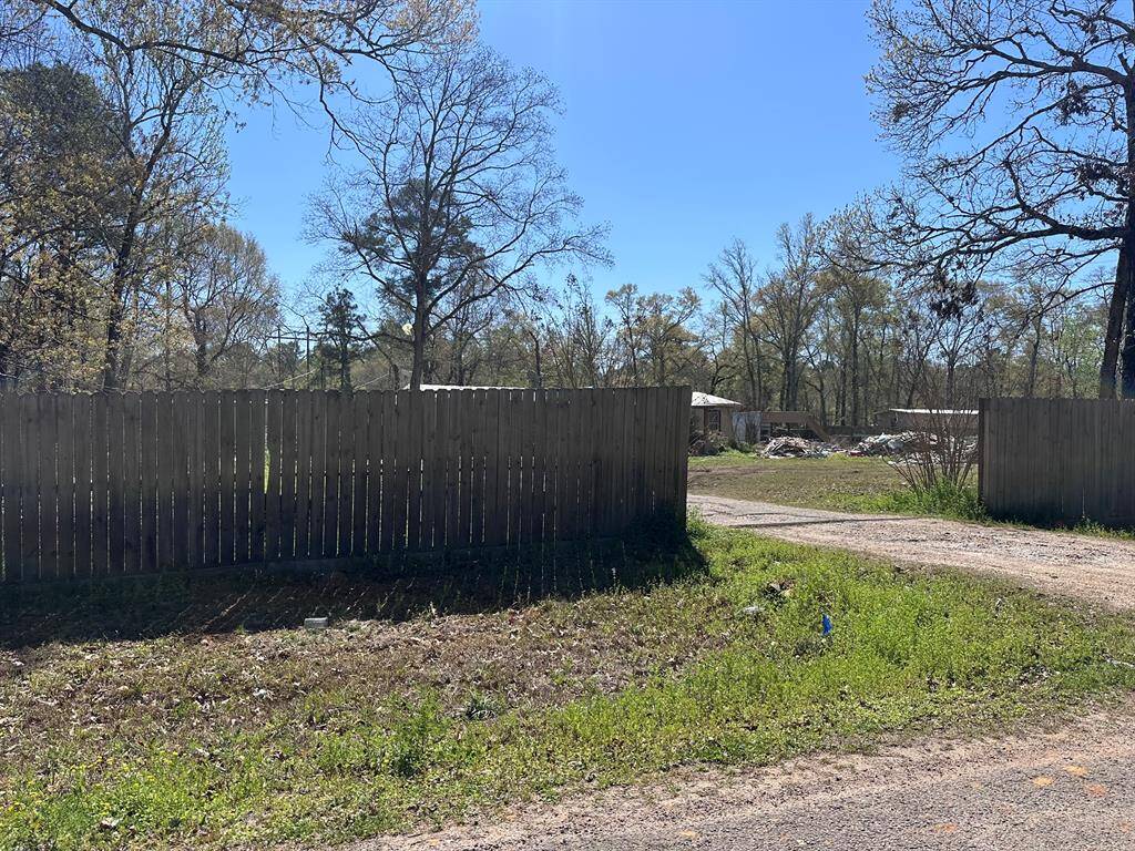 This property features a spacious lot with mature trees and a wooden fence. A gravel path leads to structures in the background, offering ample outdoor space and potential for development.