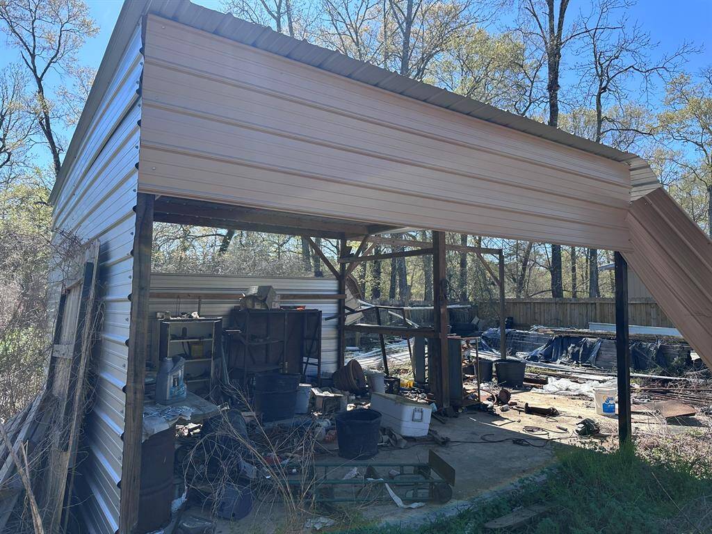 This photo shows an outdoor storage shed with metal siding, surrounded by trees. It appears cluttered with various tools and materials. Ideal for someone looking for additional storage or a workshop space on the property.