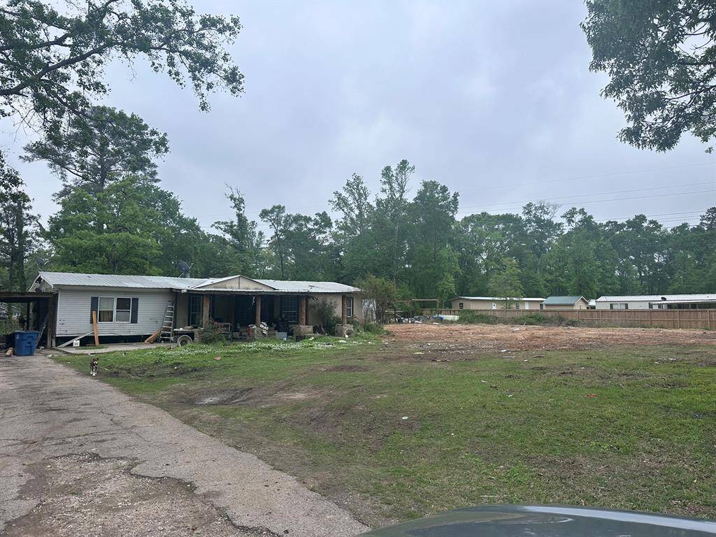 This photo shows a rural property with a single-story house and a large open yard. The house appears weathered and in need of some maintenance, with surrounding greenery and trees. The area looks spacious and serene, suitable for those seeking a quiet environment.