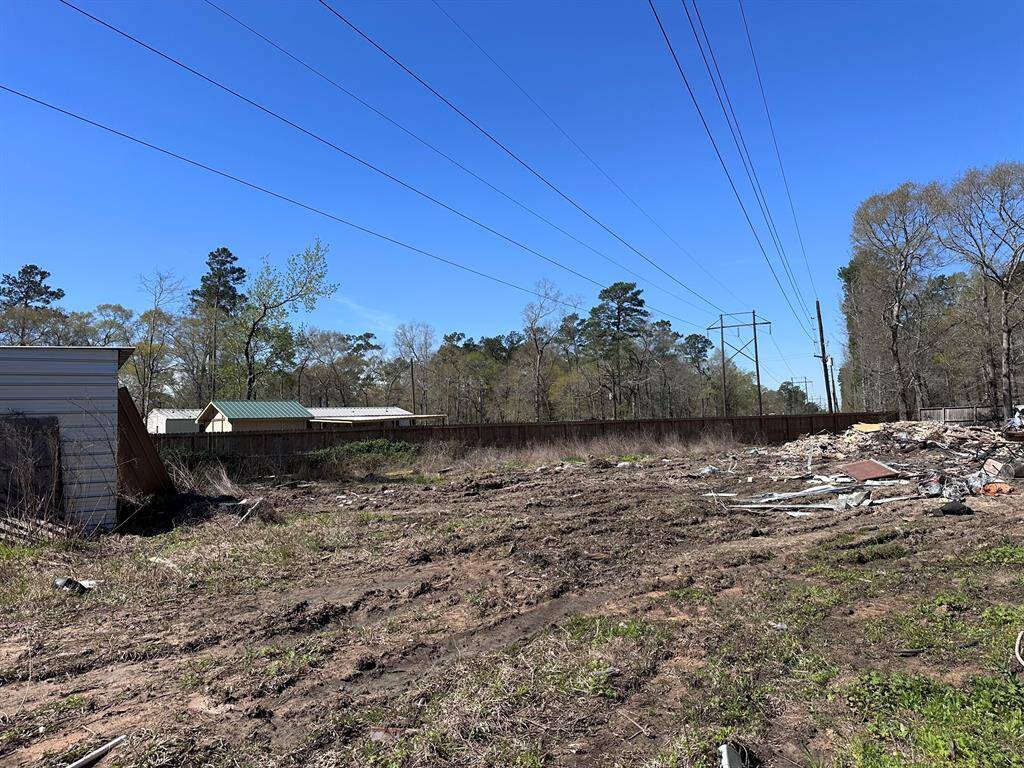 This photo shows a vacant lot with some debris and a small structure on the left. It's bordered by trees and power lines, offering a potential building site in a natural setting.