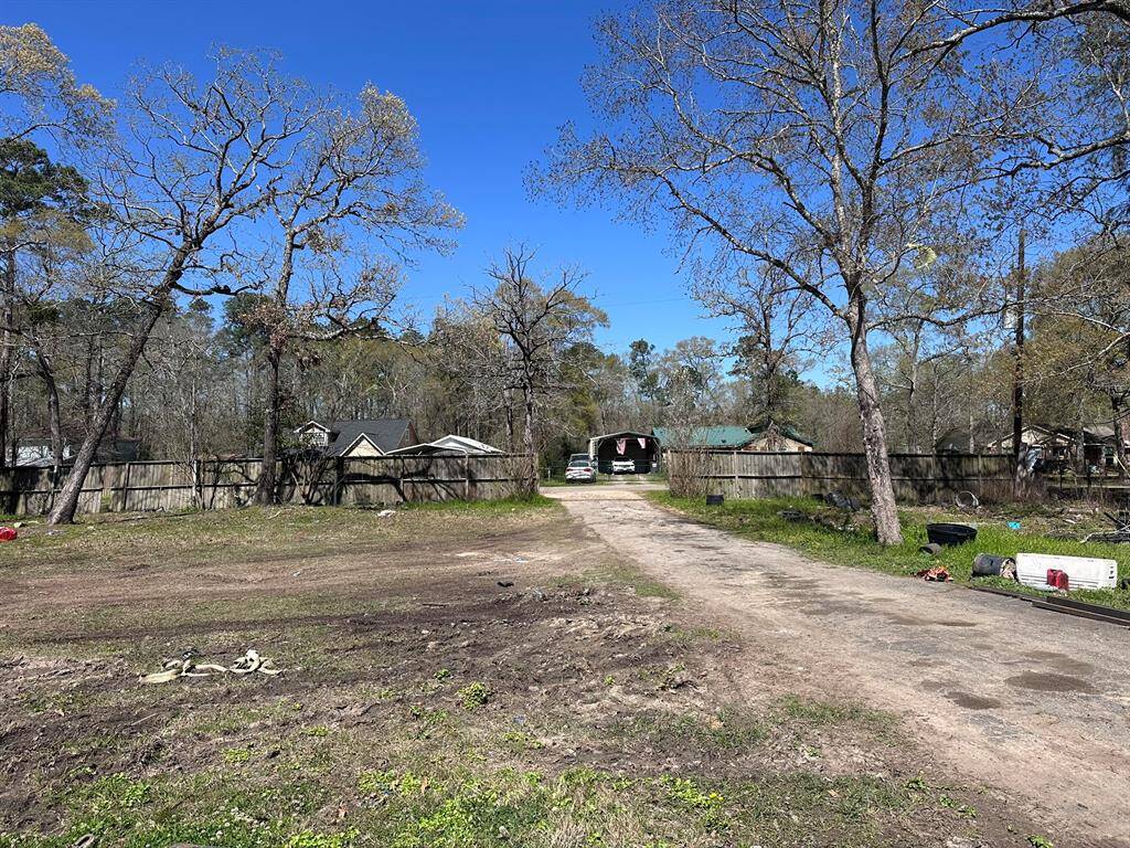 Spacious lot with a dirt driveway leading to a fenced area. Surrounded by trees, it offers a semi-rural feel with neighboring houses visible in the background. Ideal for buyers seeking a quiet, natural setting.