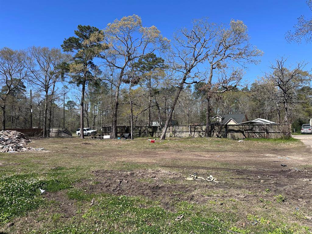 This photo shows a spacious, open plot of land with scattered trees and a clear blue sky. There's a fence in the background, and a few vehicles are visible. Ideal for building a home in a natural setting.