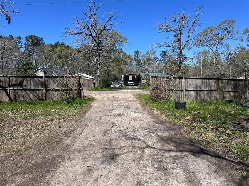 This photo shows a rural property with a dirt driveway leading to a house surrounded by trees. There are wooden fences on either side, and a couple of outbuildings are visible. The setting is serene and offers privacy.