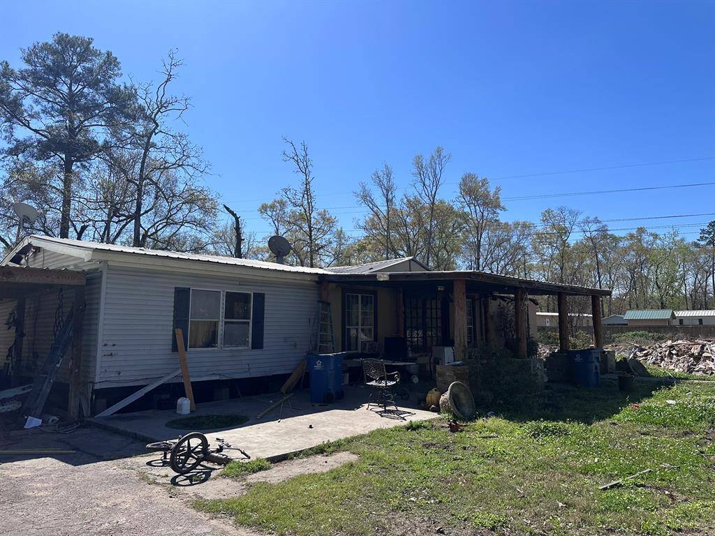This property features a single-story home with a covered porch area. The exterior shows signs of wear and may require renovation. It is situated on a spacious lot with mature trees, providing potential for landscaping and outdoor projects.
