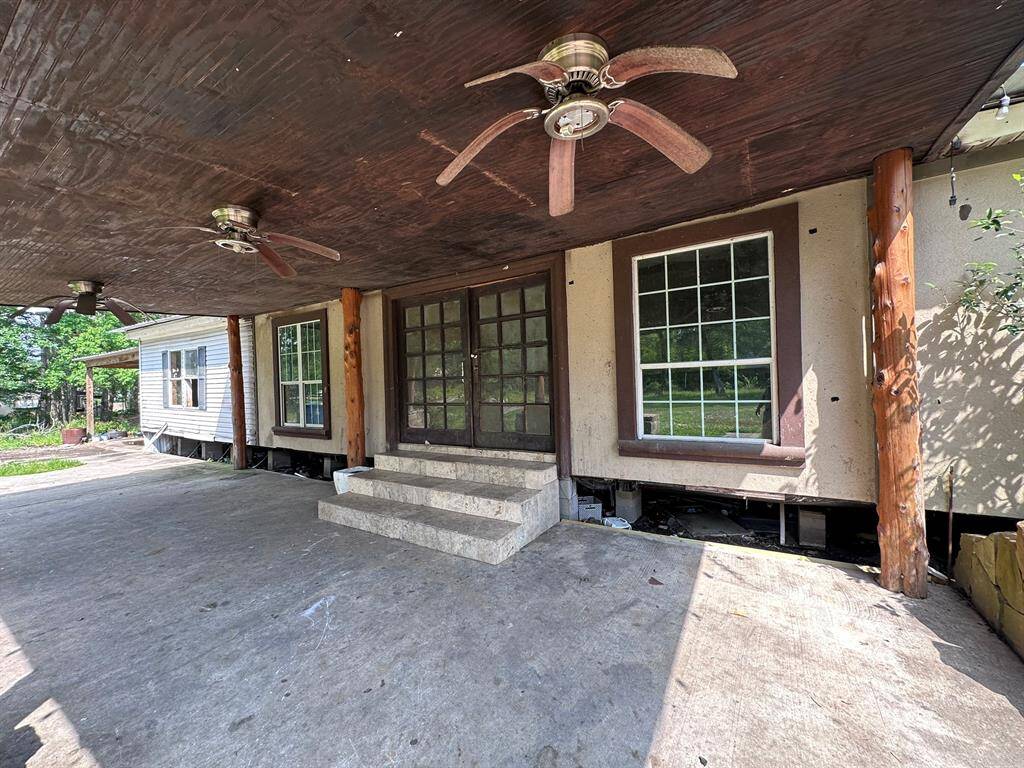 This property features a covered entryway with dual ceiling fans, rustic wooden pillars, and large windows, providing a cozy outdoor space with potential for customization.