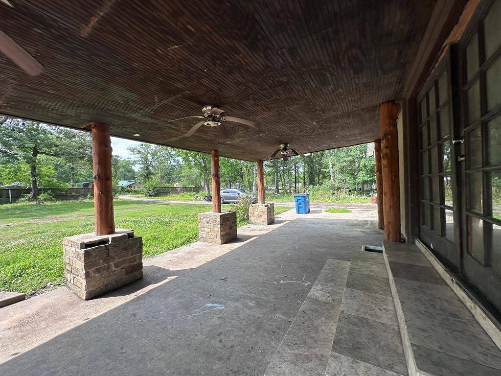 This photo shows a spacious covered patio with a wooden ceiling and ceiling fans, supported by stone pillars. It overlooks a grassy area with trees, providing a serene outdoor space.