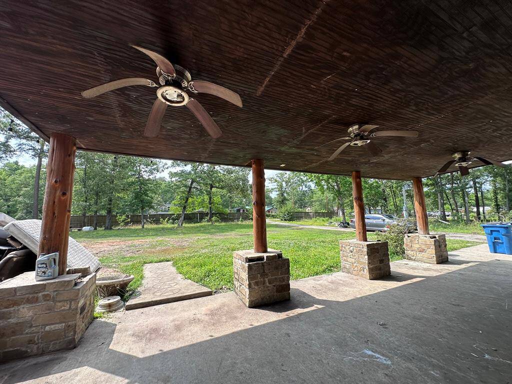 This photo showcases a spacious covered patio with ceiling fans and stone pillars, overlooking a large, grassy backyard. Ideal for outdoor gatherings and relaxation.