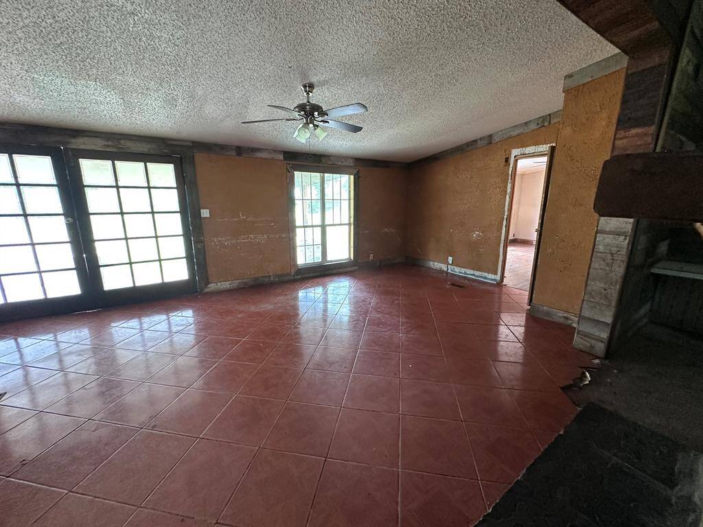 Spacious room with large windows and French doors, allowing plenty of natural light. It features a ceiling fan, tiled floors, and textured walls. Ideal for customization and renovation.