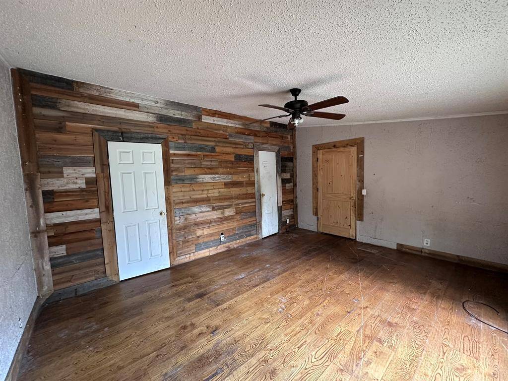 Spacious room with rustic wood paneling on one wall, hardwood floors, and a ceiling fan. Features two doors, one white and one wood, offering potential for customization.