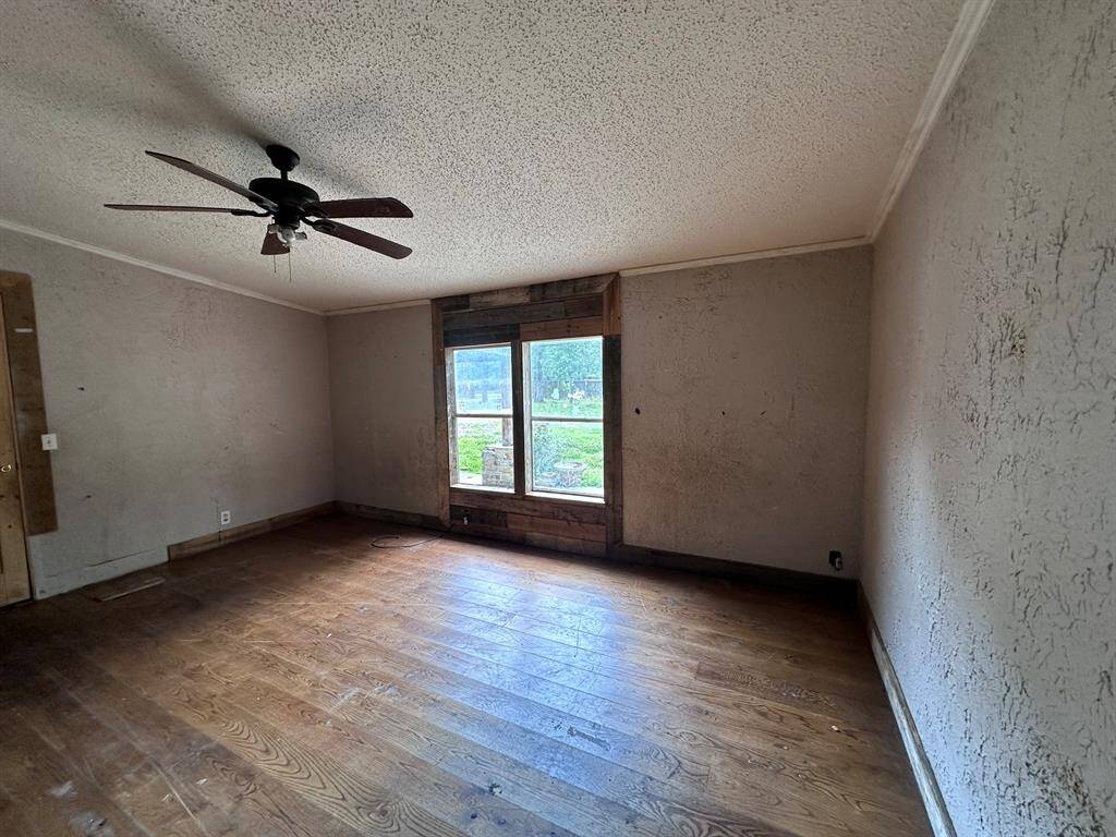 Spacious room with hardwood floors, a central window allowing natural light, and a ceiling fan. Walls may need some updating.