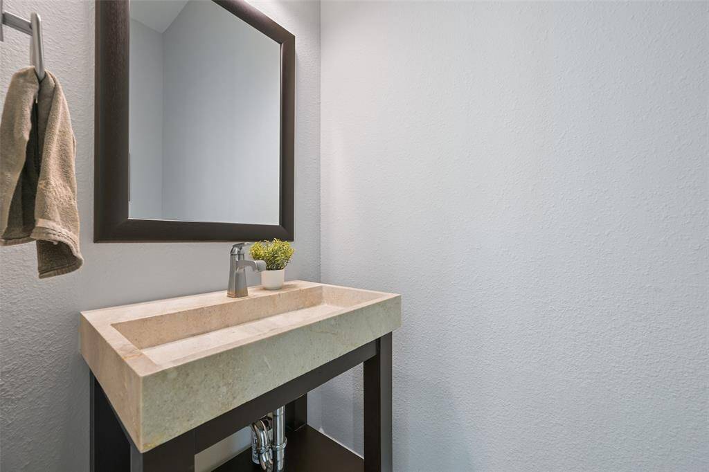 The powder room features a decorative sink, complemented by vanity lights and a stylish decorative mirror. Its convenient location makes it easily accessible from the living spaces and provides a handy option for poolside guests. This charming half-bath combines functionality with a touch of elegance