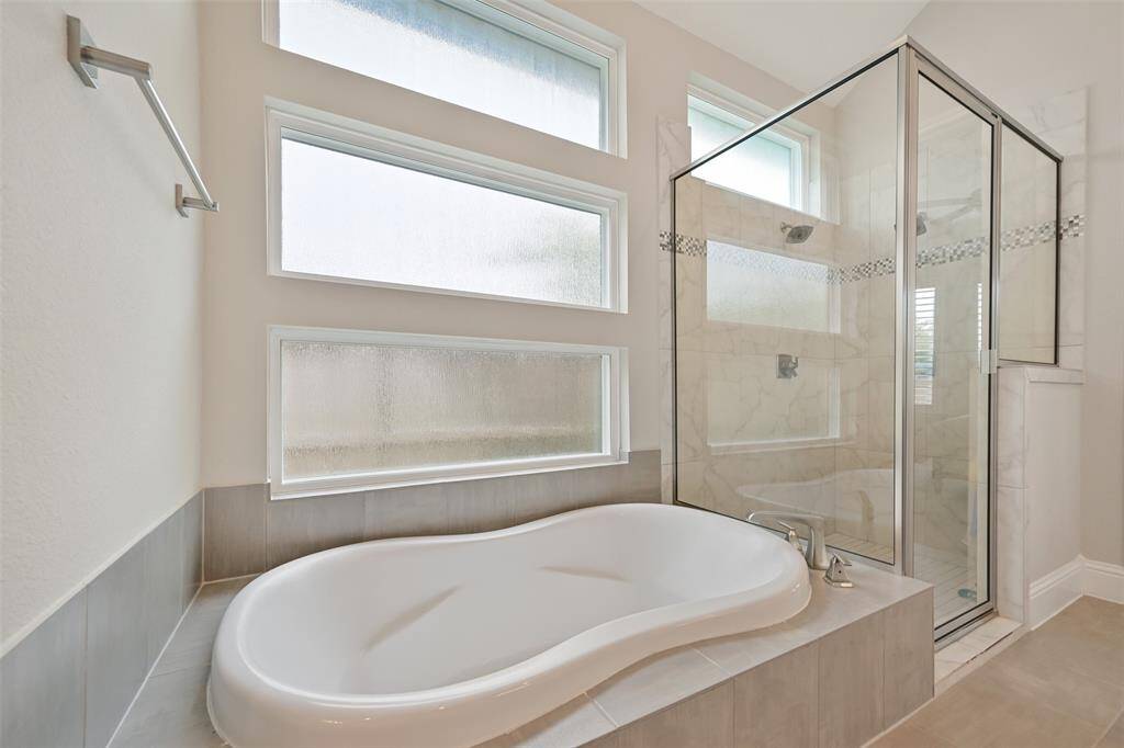 Another view of the primary bath highlighting the luxurious walk-in shower with double shower heads and a glass surround, as well as a separate soaking tub for ultimate relaxation. A large opaque window allows light while maintaining privacy.