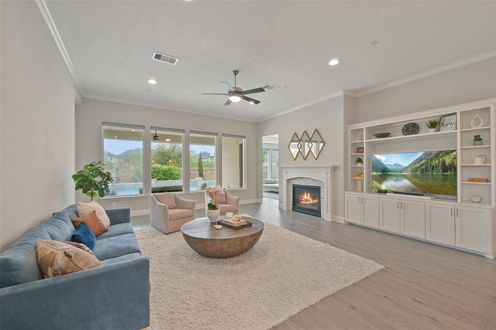 Light and bright family room is highlighted by a wall of windows w/ pull-down shades flooding the space w/ natural light and offering serene views of the covered back patio and pool. Wood-like tile floors enhance the room's warmth. The spacious room also boasts recessed can lighting, a ceiling fan/light fixture & a cozy gas log fireplace w/ a wood mantle and stone surround. Sellers have thoughtfully added a built-in media center with storage & book/display shelves, along with crown molding throughout.