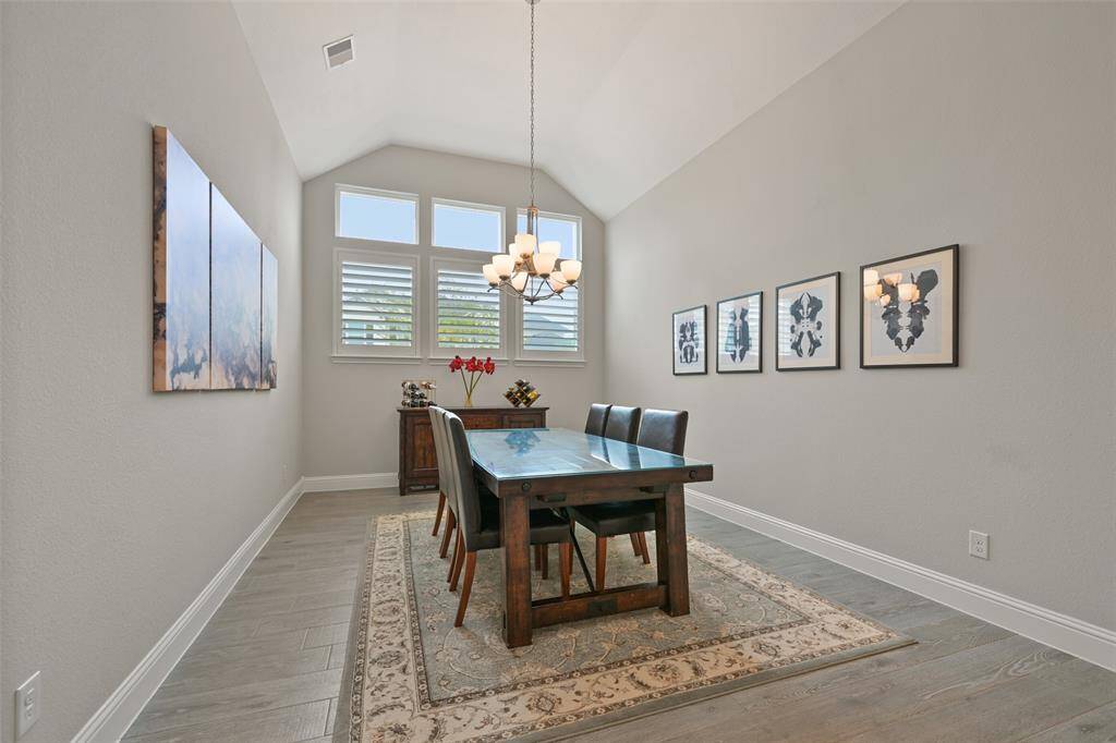 The formal dining room is generously sized, offering ample space for a large table, buffet, and plenty of wall space to showcase art. It opens seamlessly to the kitchen & family room, making it an ideal setting for entertaining. Features a vaulted ceiling that adds a sense of grandeur, complemented by a decorative light fixture. For added elegance and privacy, plantation shutters have been thoughtfully added to the windows.