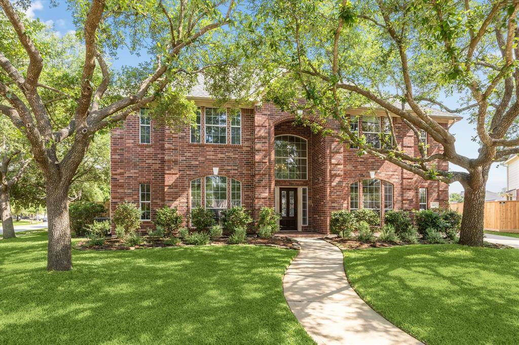 This is a charming two-story 3420 sqft brick home with a welcoming entrance, surrounded by mature trees and a well-manicured lawn. The front path curves gracefully to the door, and large windows provide ample natural light.