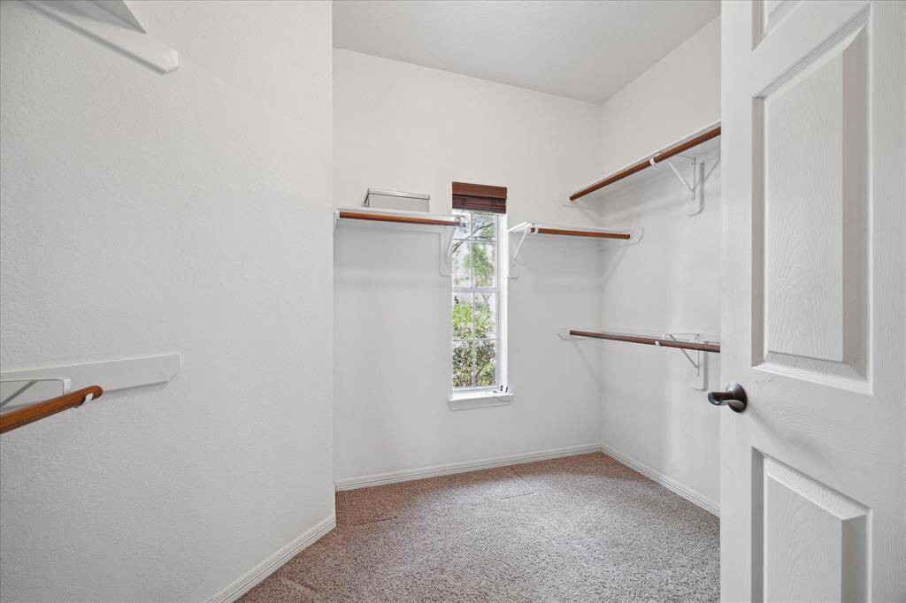 This photo features a bright, spacious walk-in primary closet with multiple wooden shelves and a window for natural light, offering ample storage space. This is only one of 2 large closets in the primary bathroom