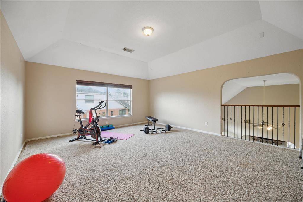 Spacious, carpeted loft area/game room with a vaulted ceiling, ideal for a home gym or recreational space. Features a large window for natural light and overlooks the floor below through an open railing.