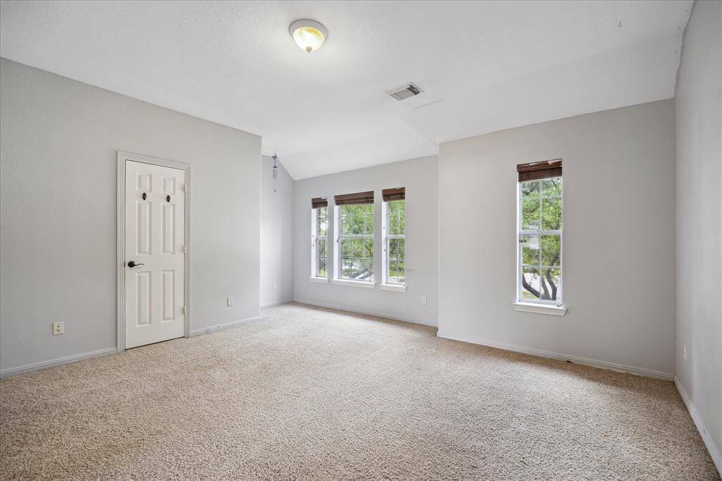 This room is spacious with neutral walls and carpet, featuring three large windows that provide ample natural light. It includes a simple ceiling light fixture and a closed door, making it a versatile space for various uses. This secondary bedroom has a full bathroom shared by the game room upstairs to the left of the staircase.