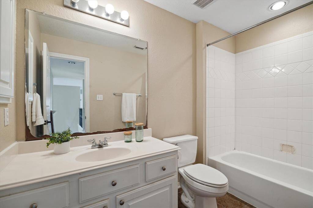 This bathroom features a clean, neutral design with a large mirror, vanity with ample storage, and a classic white tiled shower-tub combo. Bright lighting enhances the space, making it feel open and inviting. This is the bathroom off the secondary bedroom at the landing of the staircase on the second floor.
