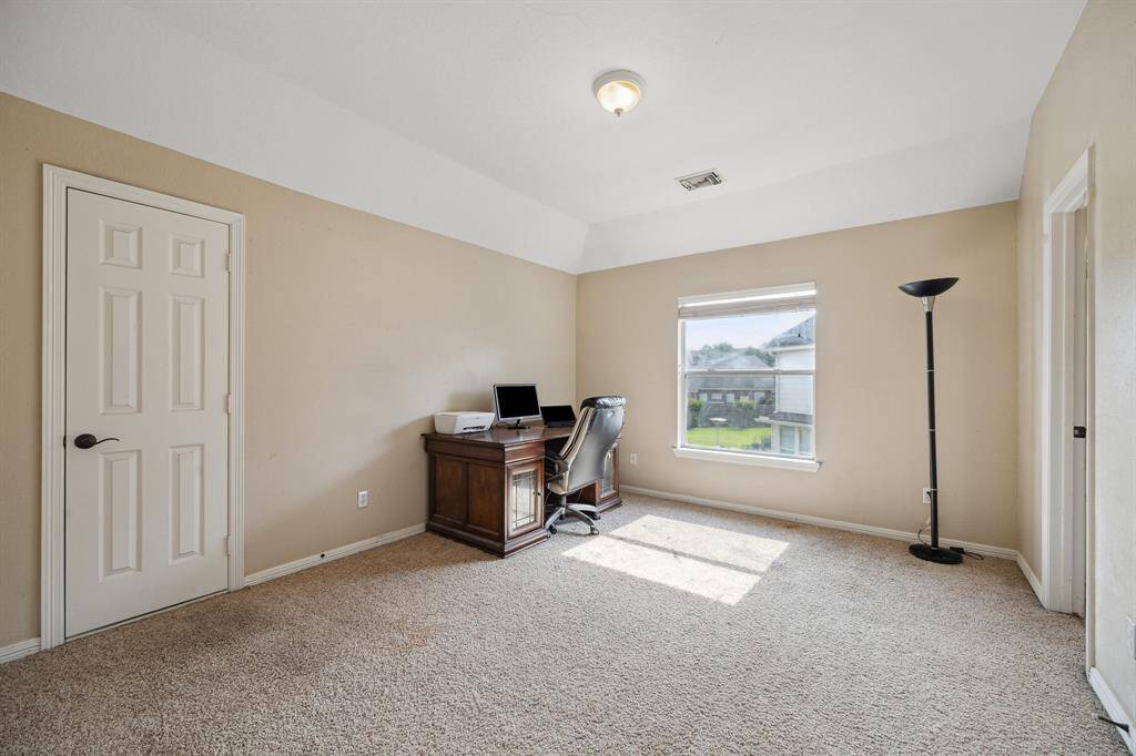 This spacious kitchen features stainless steel appliances, ample wooden cabinetry, and a large island. Natural light flows through arched windows, complementing the tile flooring. A dining area at the end offers a welcoming view of the backyard.