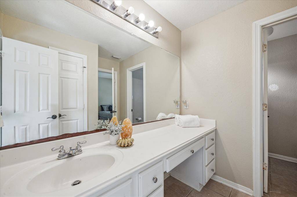 This bathroom features a large mirror with vanity lighting, a single sink with a spacious countertop, and neutral-toned walls and tiles. It offers plenty of storage with multiple drawers, creating a clean and functional space. This is the jack and jill bathroom adjoining two large secondary bedrooms. The toilet and tub/shower is seperate