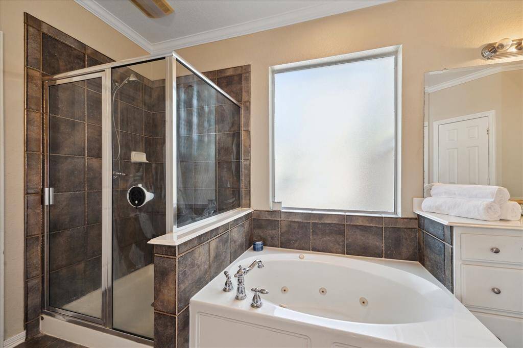 This bathroom features a spacious glass-enclosed shower and a luxurious jetted bathtub with dark tile accents, complemented by a large frosted window providing natural light and privacy.