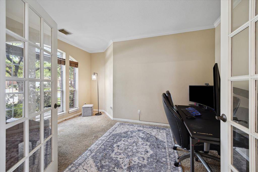 This spacious living room features high ceilings, a large ceiling fan, and an open second-floor balcony. It includes a cozy fireplace, modern gray seating, and ample natural light from a large window. A central staircase adds elegance, and neutral tones create a warm, inviting atmosphere.