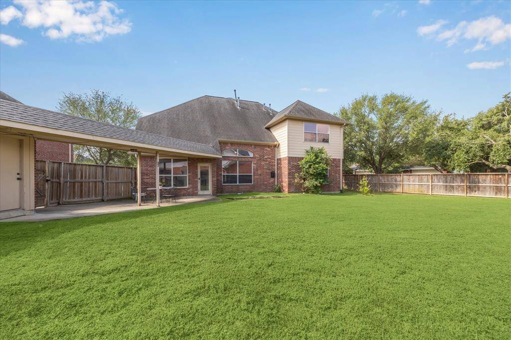 This photo showcases a backyard with a covered patio and a seating area, set against a well-maintained lawn. The space is bordered by a wooden fence and features a brick exterior, providing a private and inviting outdoor area.