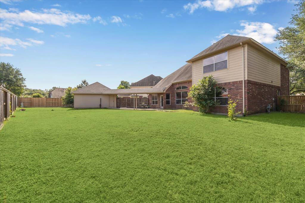 Spacious backyard with lush grass, featuring a two-story brick house. There's a covered patio area and wooden fencing, ideal for privacy and outdoor activities. Ample space to build a pool. almost 1/4 acre of land