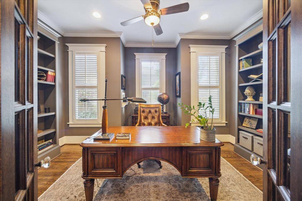 This home office offers a sophisticated setting for work or reflection. Three oversized windows with classic millwork allow natural light to balance the room’s rich, moody palette, while plantation shutters offer privacy.
