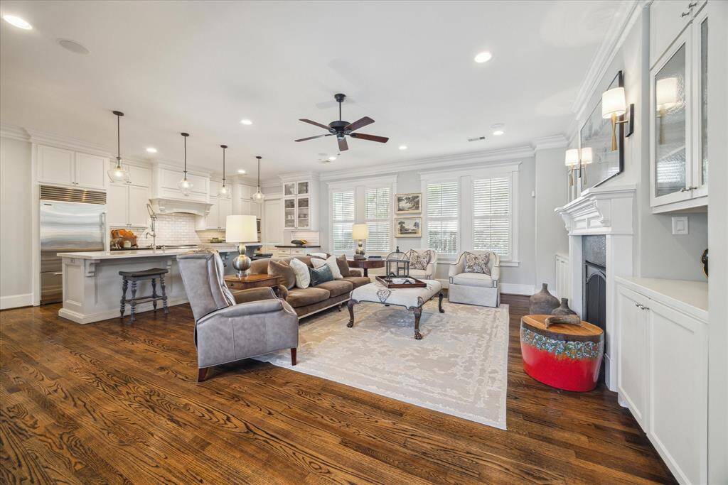 Spacious and light-filled living area has custom millwork, built-in cabinetry, and a central fireplace with detailed surround. Reclaimed oak floors and crown molding add warmth and character, while the windows provide abundant natural light. The open flow connects seamlessly to the chef’s kitchen, featuring pendant lighting, a large island, and professional-grade appliances—perfect for entertaining or everyday living.