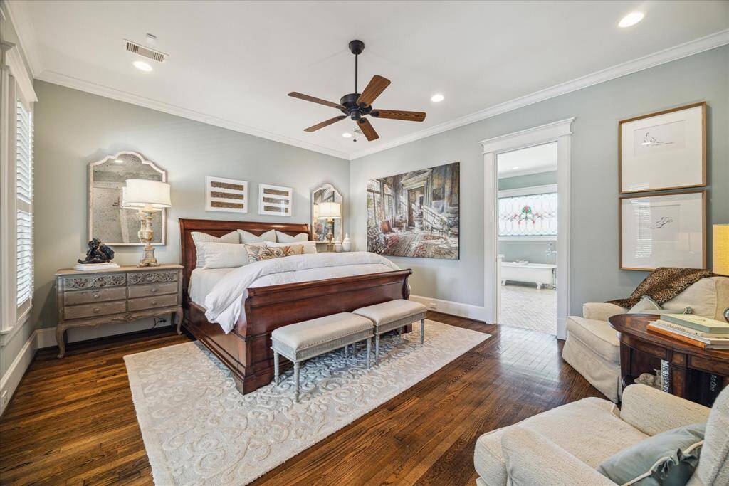 A serene retreat, the primary suite features hardwood floors, elegant crown molding, and abundant natural light. The generous layout comfortably fits a king-sized bed with room to lounge, while the windows provide a view of the covered porch.  Through the doorway, a glimpse of the spa-like bathroom teases what’s to come—including the show-stopping original clawfoot tub set beneath a stained-glass window.