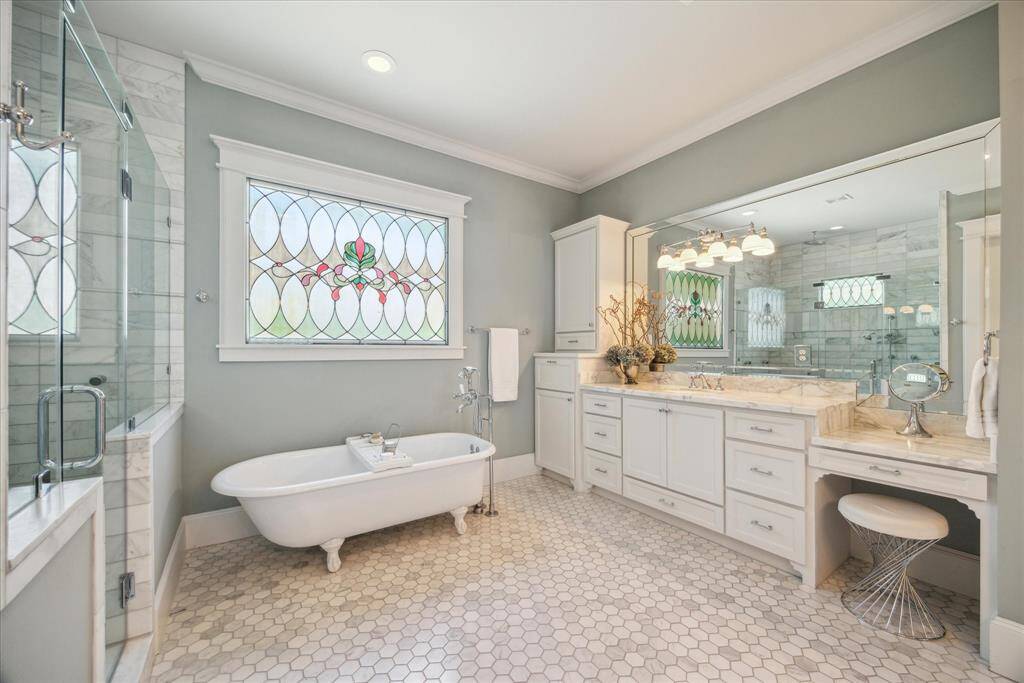 A spa-worthy sanctuary wrapped in timeless design, the primary bath is anchored by a stunning original clawfoot tub set beneath a hand-crafted stained glass window. Marble hex tile underfoot, dual vanities with marble countertops, and a glass-enclosed shower lined with marble surround offer both elegance and everyday ease. Custom cabinetry and a dedicated vanity area add functionality, while every finish speaks to thoughtful craftsmanship and quiet luxury.