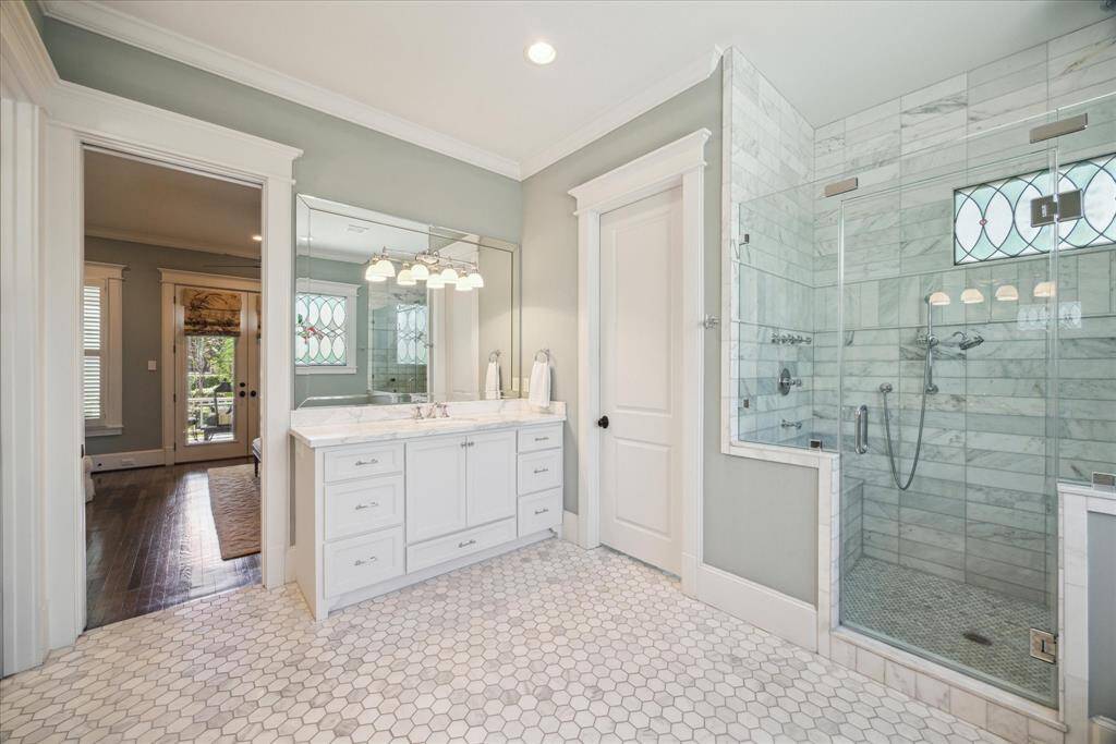 Every surface of the primary bath speaks to quality. The marble-clad shower, with its frameless glass enclosure, features dual shower heads, a built-in bench, and a stained-glass privacy window that mirrors the home’s historic charm.