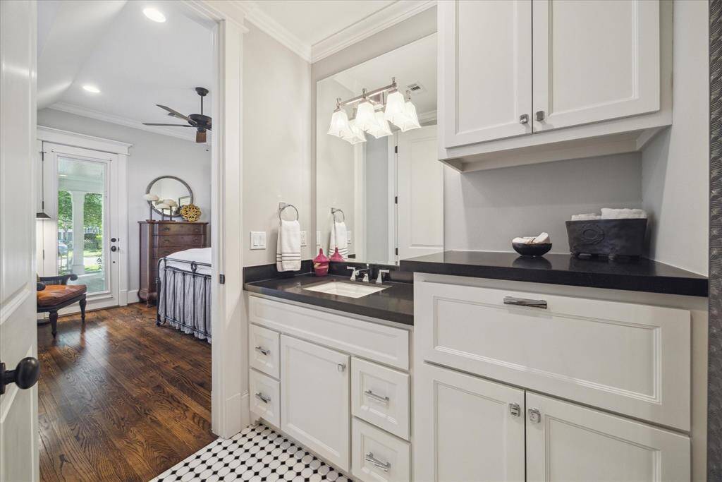 A crisp, timeless palette elevates this guest bath.  Featuring shaker-style  cabinetry, sleek black countertops, and polished chrome hardware, the space blends transitional design with subtle drama. The hex tile floor nods to vintage charm, while integrated upper cabinets and expansive vanity drawers offer elevated function with a custom-built feel. Not shown is a deep bathtub.