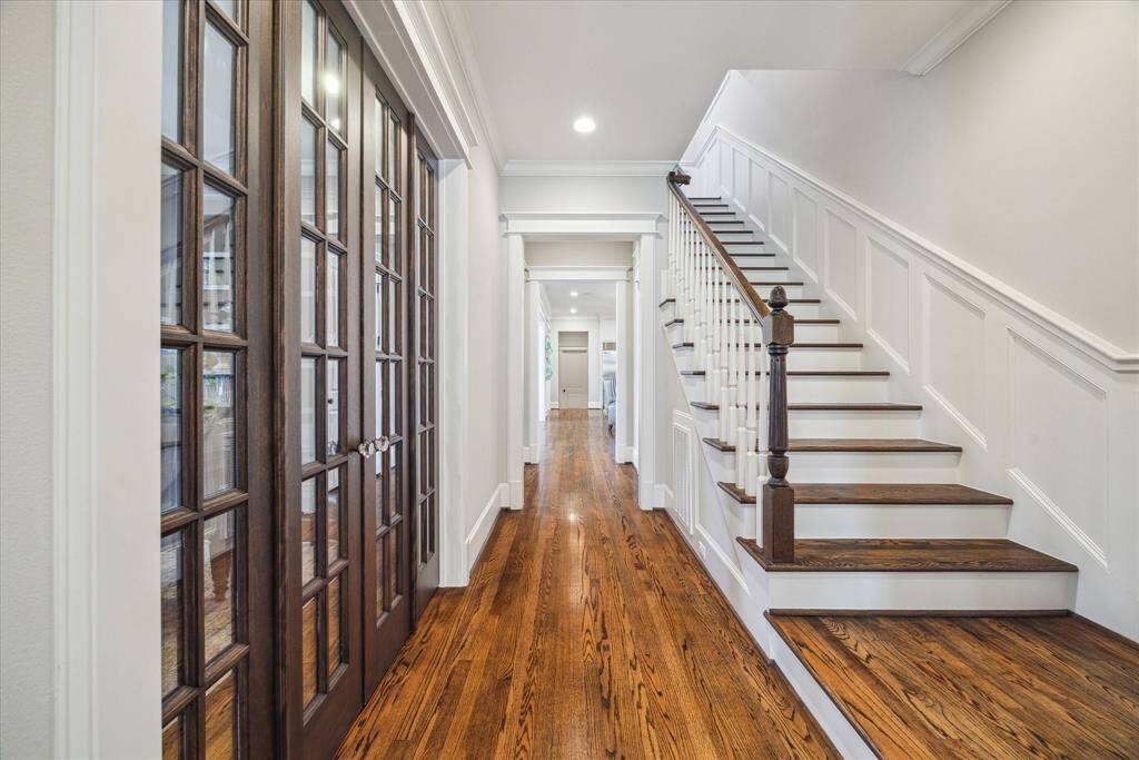 A gallery-style entry anchored by gleaming hardwoods and timeless millwork sets the tone for everything that follows. To the left, rich wood French doors open to a home office or study while straight ahead, the view extends all the way through to the kitchen, inviting you deeper into the home.