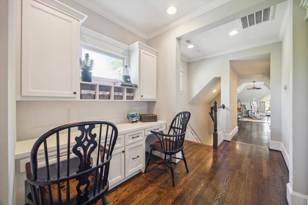 Tucked along the upper landing, this dual workstation offers a stylish, built-in solution for productivity without sacrificing aesthetics. Custom cabinetry, inset paneling, and crown molding makes the design intentional and architectural, not just functional. A transom-style window ushers in soft natural light.