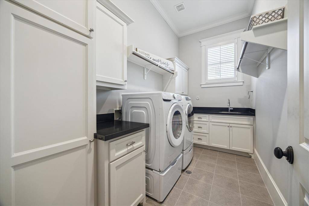 Framed in custom cabinetry with black stone counters and a deep utility sink, this laundry room is both polished and practical. Upper cabinets offer clean storage, while the built-in folding shelf and drying rod make organization effortless. Natural light filters through a classic framed window, giving the room a bright, airy flow that turns chores into moments of calm.