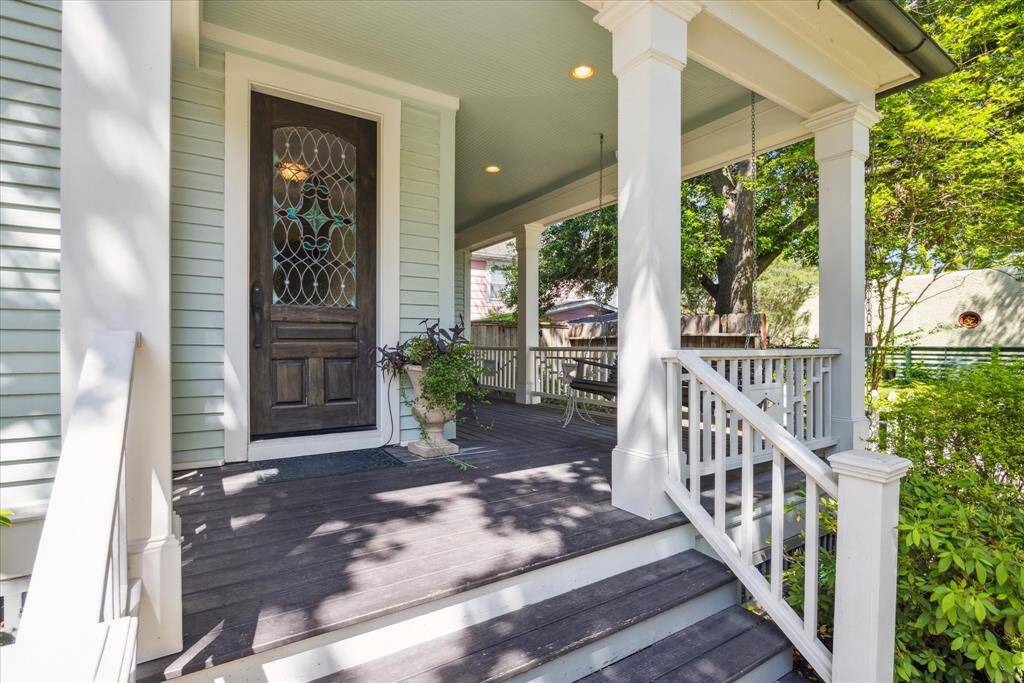 The front porch at 1539 Rutland blends historic detail with everyday livability. A rich wood front door with leaded glass anchors the entry, while the painted beadboard ceiling and crisp white columns add classic character.