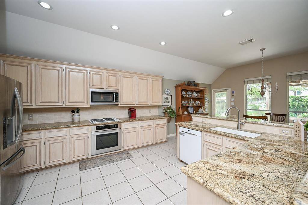 Bright and functional, the kitchen features an expansive layout with ample counter space, classic tile backsplash, and recessed lighting. The open concept ensures connectivity to the adjacent dining area and backyard views.