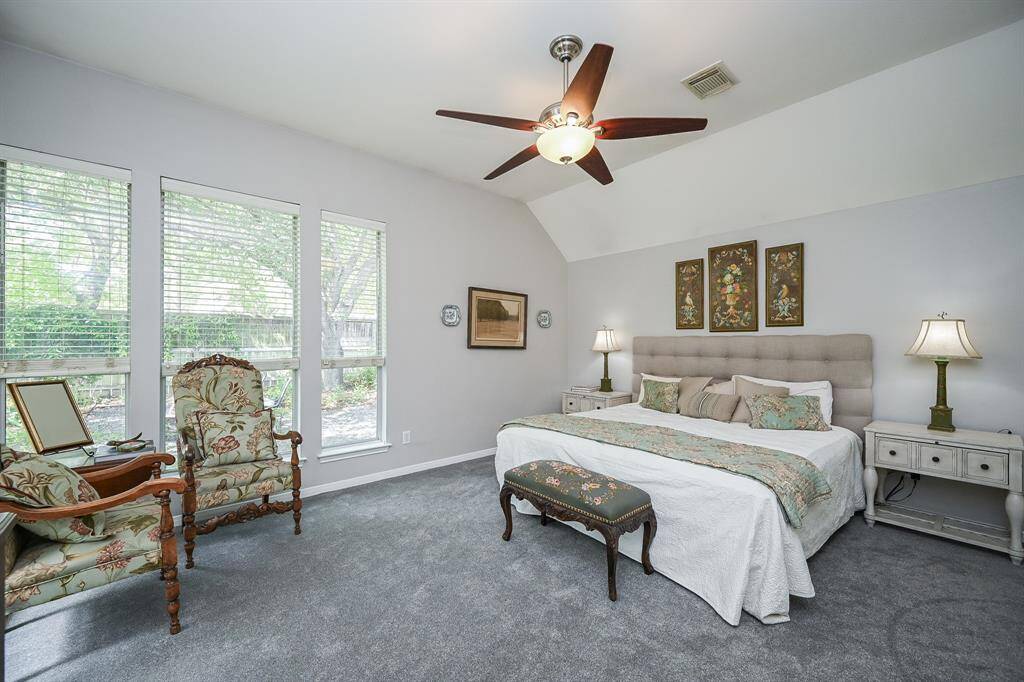 The serene primary suite features soft carpeting, high ceilings, and a wall of windows with views of the lush backyard.