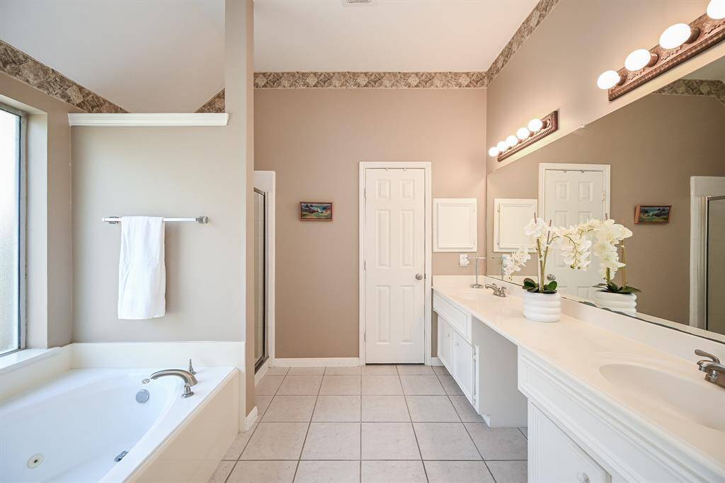 Start and end your day in this bright and inviting primary bath, complete with dual vanities, ample counter space, and soft lighting.
